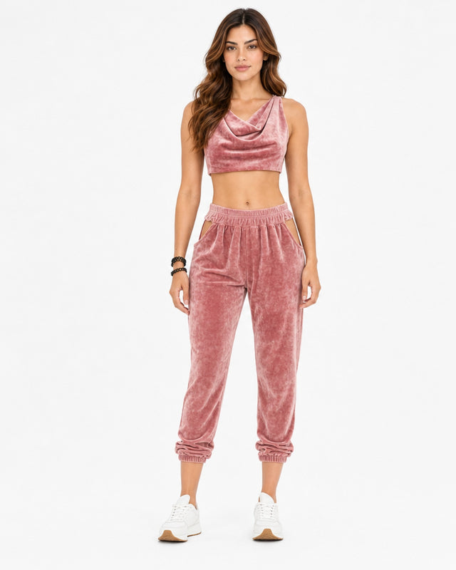 A model wearing a sleeveless, draped crop top and matching joggers in a pink fabric.