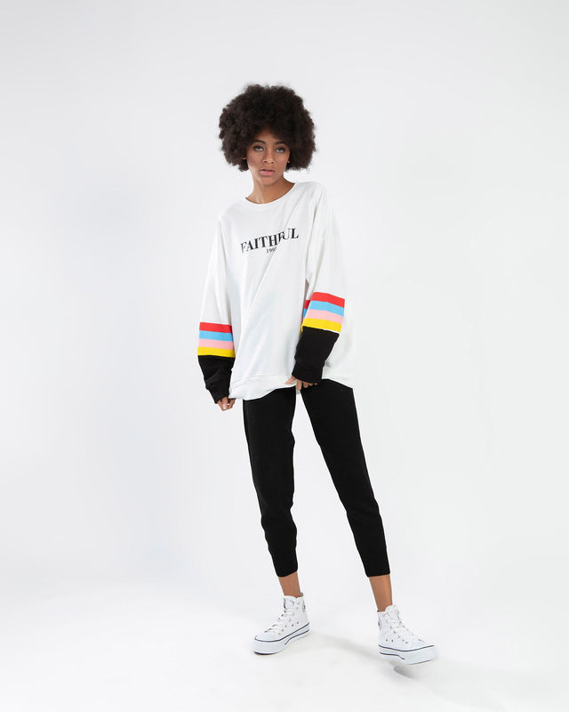 Model in White Faithful 1995 Oversized Long Sleeve Top with Colorful Striped Sleeves and Black Joggers.