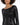 A close-up of a woman wearing a fitted black sequin dress with long sleeves and a boat neckline.