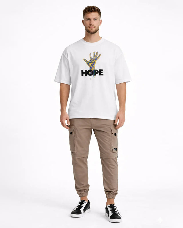 A man stands wearing a white oversized t-shirt with a colorful hand graphic and the word "HOPE," paired with beige ca...
