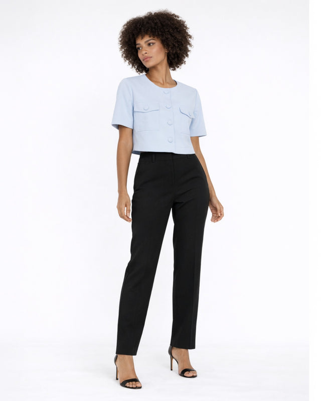A model poses in a light blue cropped top with button details and two front pockets, paired with black trousers.