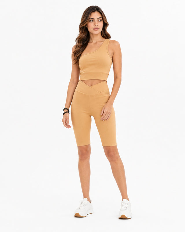 A model poses in a fitted, ribbed crop top and matching high-waisted bike shorts in a beige tone.