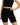 A model poses in a fitted black crop top and matching high-waisted shorts, showcasing a sleek, minimalist style.