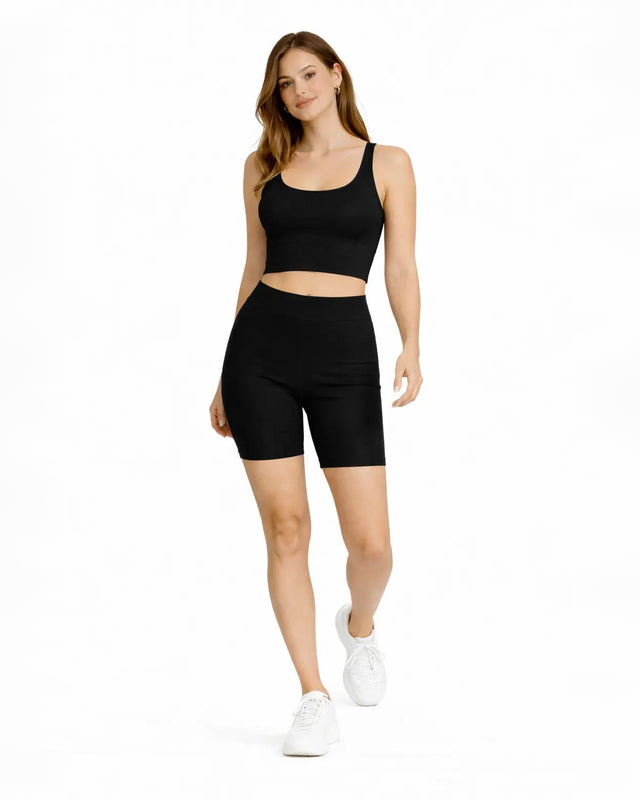 A woman wearing a black crop top and matching high-waisted shorts, paired with white sneakers, walking confidently.