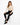 A model sits on a white cube, wearing a fitted beige long-sleeve top with cutouts and black skinny jeans.