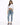 A woman stands confidently in a cropped white long-sleeve top, light blue jeans, and gray fuzzy slippers.