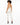A model with curly hair wears a beige bodysuit and white fitted pants, showcasing a stylish back design.