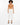 A model wearing a fitted, tan bodysuit paired with tailored white pants and black strappy heels.