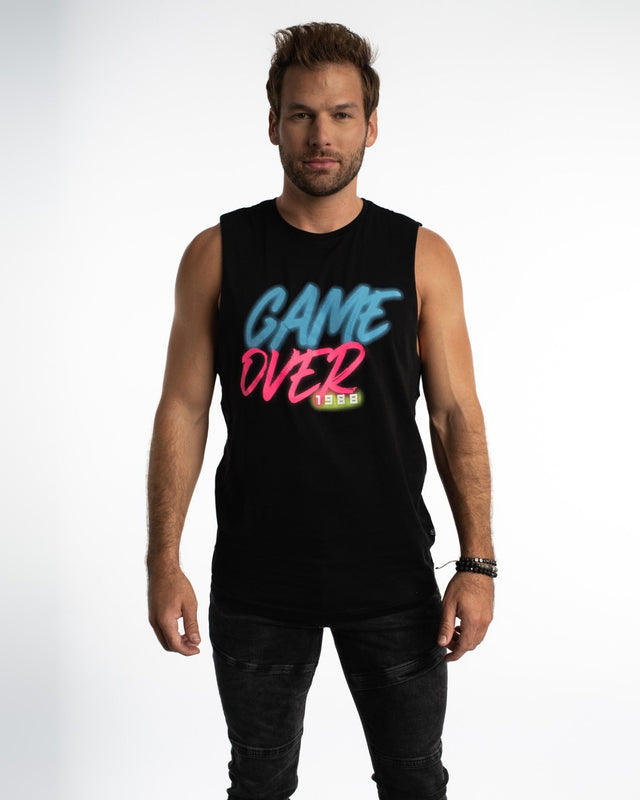 A man wearing a black sleeveless shirt with colorful "GAME OVER 1988" graphic design, paired with dark jeans.
