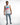 A man stands confidently in a sleeveless white top with colorful text, paired with distressed light blue jeans and ca...