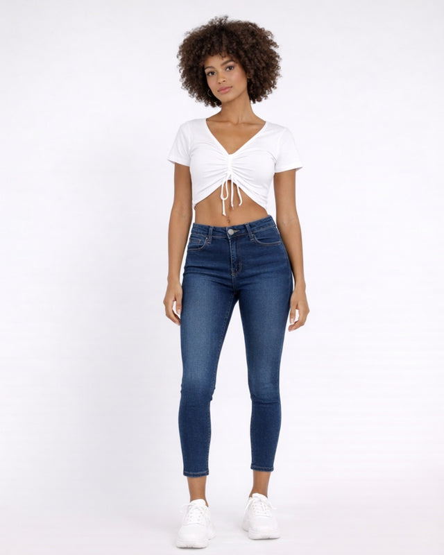 A model wearing a white cropped top and blue skinny jeans, paired with white sneakers, standing against a light backg...