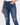 Close-up of a person wearing dark blue ripped jeans with a high waist and a hand in the pocket.
