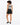 A woman with curly hair wears a patterned bodysuit and high-waisted black shorts, standing with her back to the camera.