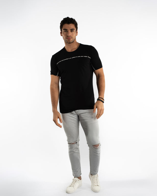Man in Odin light grey distressed jeans with ripped knees and a black streetwear graphic t-shirt.