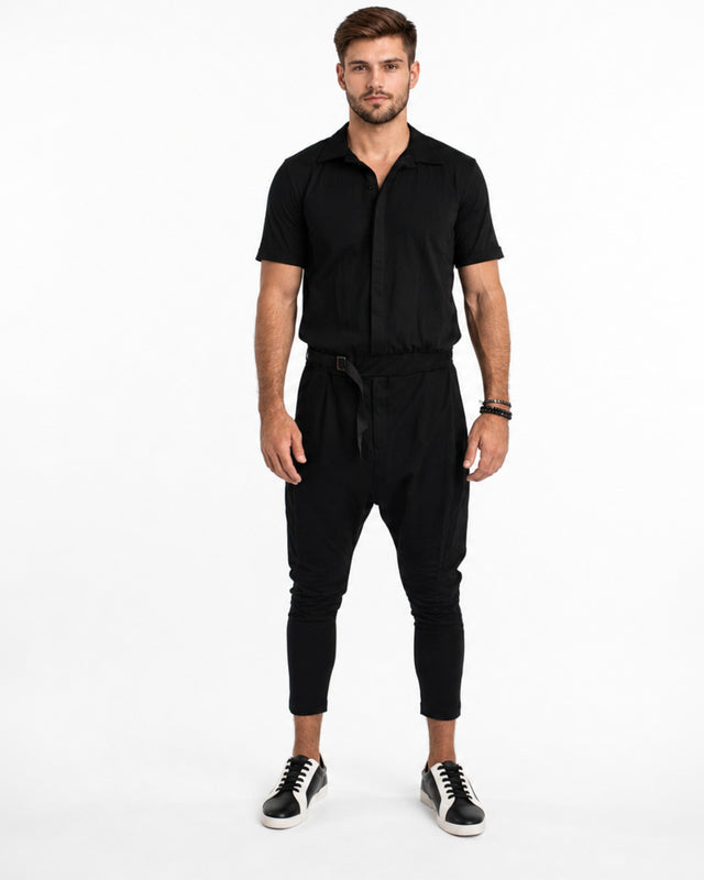 A man stands confidently in a black short-sleeve overall with tapered legs and stylish sneakers.