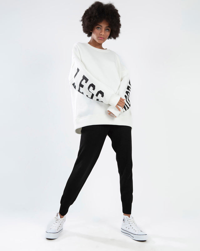 Model wearing the Ari white oversized sweatshirt with black sleeve lettering, black joggers, and white sneakers.