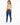 A woman with long hair wears a light green cropped top and high-waisted blue jeans, standing in profile.
