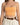 A close-up of a woman wearing a fitted orange crop top with thin straps, paired with high-waisted beige trousers and...