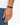A close-up of a hand wearing a minimalist black bracelet with a sleek clasp, set against a light background.