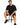 A man sits on a black stool wearing a loose-fitting black t-shirt and matching shorts, paired with black sneakers.