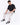 A man sits on a white cube wearing light-colored pants, a black shirt, and stylish black sneakers.