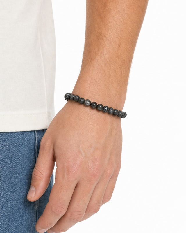 A close-up of a hand wearing a dark beaded bracelet, showcasing a casual style against a light shirt.