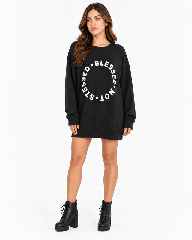 A woman stands wearing a black oversized sweatshirt with a circular white text design, paired with black chunky boots.