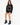 A woman sits on a stool wearing a black sweatshirt with bold white text and stylish black heeled boots.
