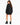 A woman with long hair wears a loose black sweatshirt dress and chunky black heeled boots, facing away.