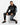 A man sits on a white cube wearing black sweatpants with graphic prints and a matching hoodie, paired with black snea...