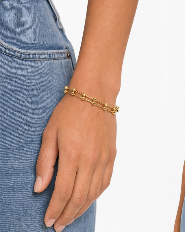 A gold bracelet with spherical beads, elegantly worn on a hand against a denim background.
