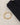 Gold bracelet with geometric links and a lobster clasp, placed beside a folded black garment on a textured surface.