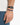 A close-up of a hand wearing a colorful beaded bracelet alongside a black watch.