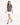 A woman walks confidently in a gray tee with a stylish graphic, paired with a white skirt and black heels.
