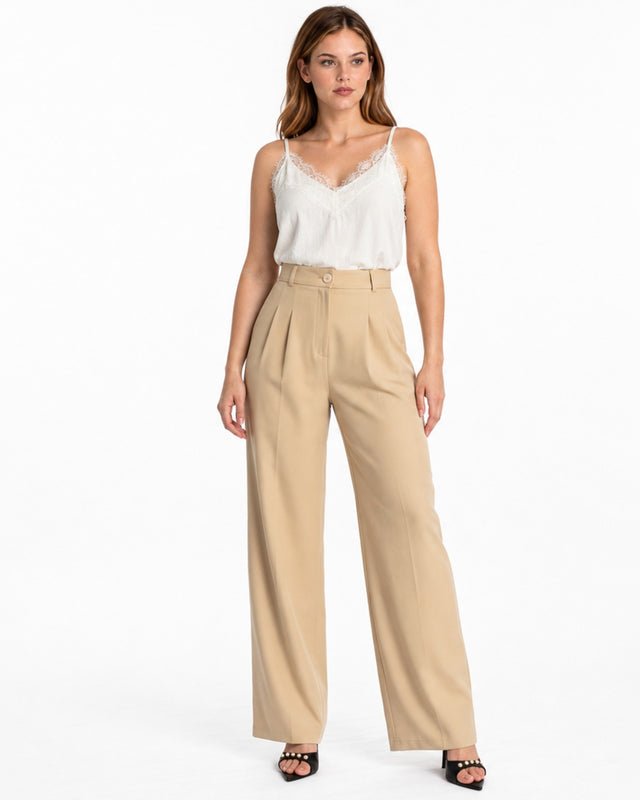 A woman stands confidently in beige high-waisted pants paired with a delicate white lace camisole.