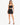 A woman poses in a black crop top and matching mini skirt, showcasing a stylish, fitted look with strappy heels.