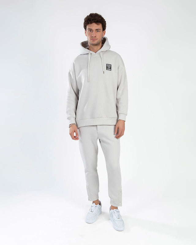 Man wearing Rostory light grey streetwear co-ord set with oversized hoodie and joggers with snap-button ankle cuffs.