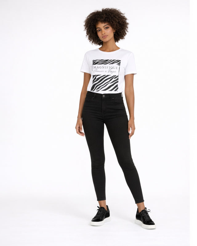 A model stands confidently in a graphic tee and black skinny jeans, paired with stylish black sneakers.