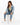 A woman with long, wavy hair sits on a white cube, wearing a denim jacket, cropped top, and light blue jeans.