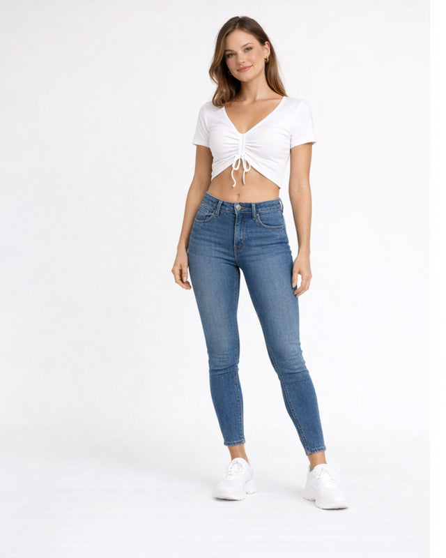 A woman stands confidently in a cropped white top and fitted blue jeans, paired with white sneakers.