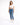 A woman stands confidently in a cropped white top and fitted blue jeans, paired with white sneakers.