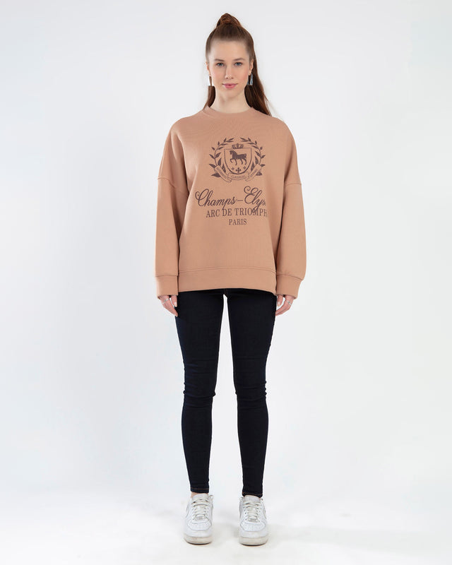 Model wearing Champs-Élysées brown oversized sweatshirt with graphic crest, black skinny jeans, and white sneakers.