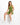 A model sits on a white cube wearing a fitted olive green one-shoulder top and matching shorts with white sneakers.
