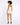 A model with curly hair poses from the back in a light-colored, sleeveless romper and black heels.