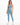 A woman stands confidently in a light blue one-shoulder crop top and matching leggings, paired with white sneakers.