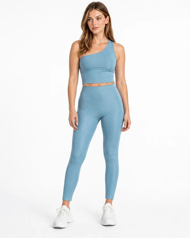A model wearing a light blue one-shoulder crop top paired with matching leggings and white sneakers.