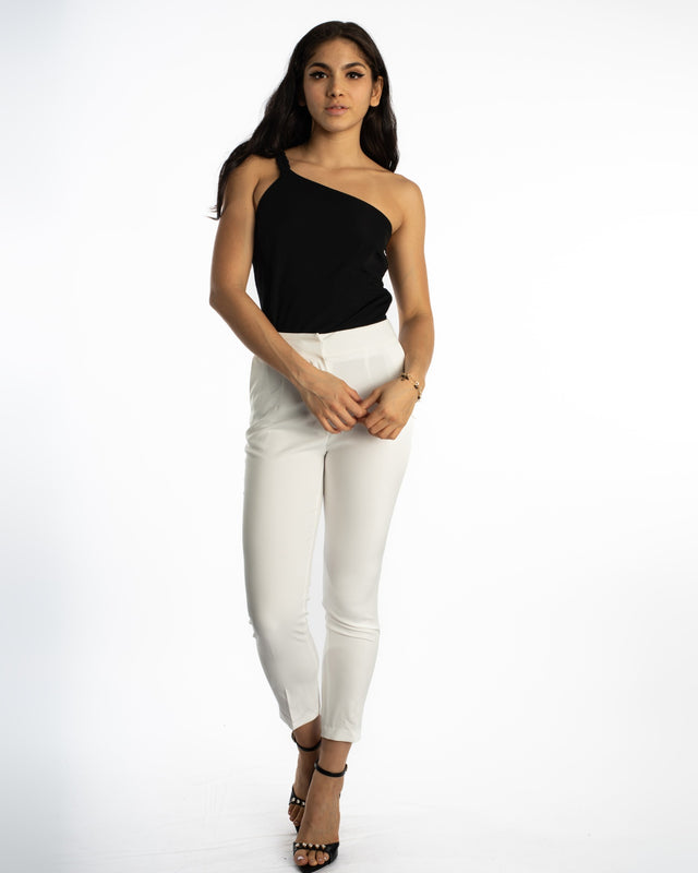 A model poses in a black one-shoulder top paired with white fitted pants and strappy black heels.