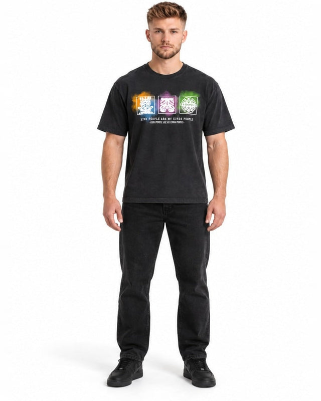 A man stands wearing a black graphic t-shirt featuring colorful designs and a positive message.