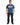 A man stands wearing a blue graphic t-shirt featuring colorful designs and a playful slogan, paired with black jeans.