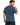 A man with short brown hair and a beard is wearing a blue t-shirt, looking back over his shoulder.